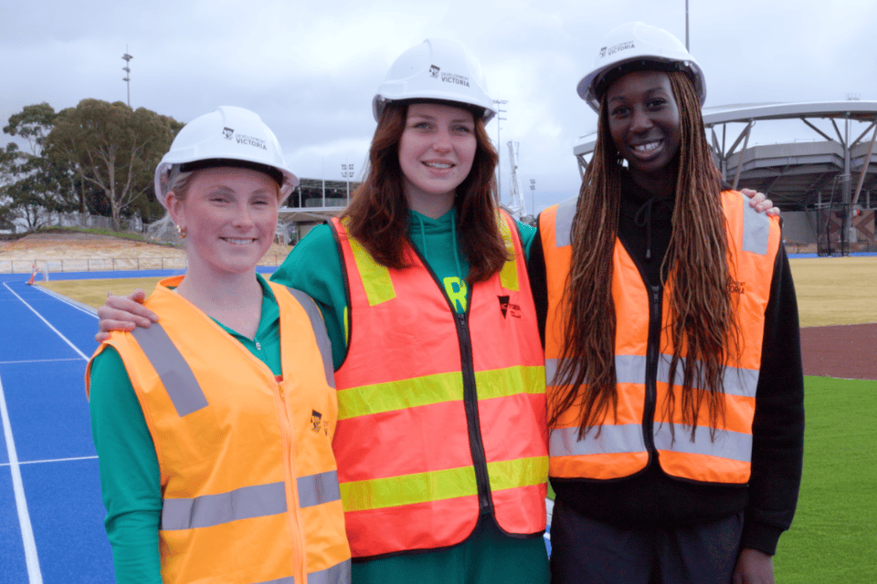 Three women wearing PPE on athletics track