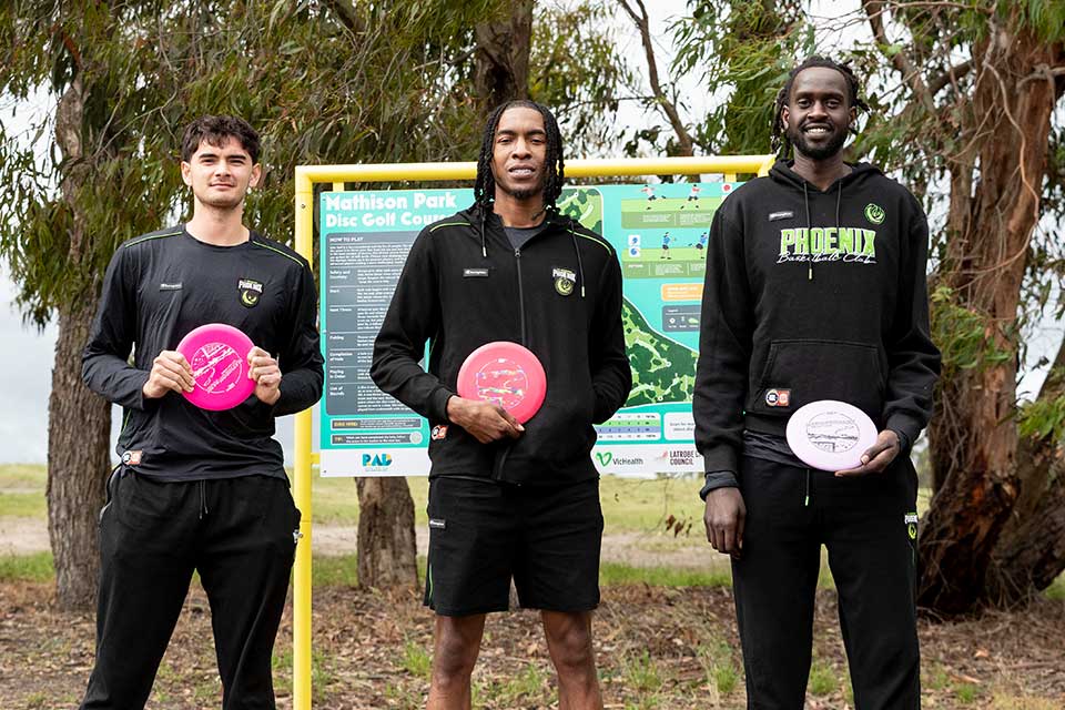 Players from the South East Melbourne Phoenix pose with frisbees next to a frizbee golf target. 