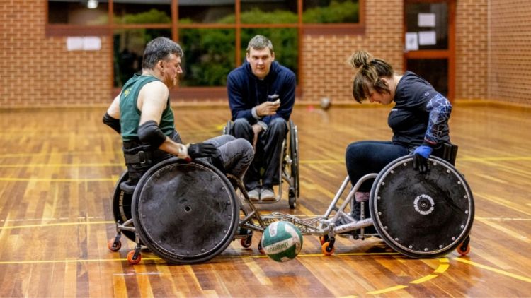 A male and female player and a referee, participate in a wheelchair basketball game.