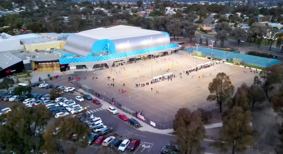 Artist's impression of Bendigo Stadium including the main buildings in the background and a carpark and people playing netball under lights in the foreground.