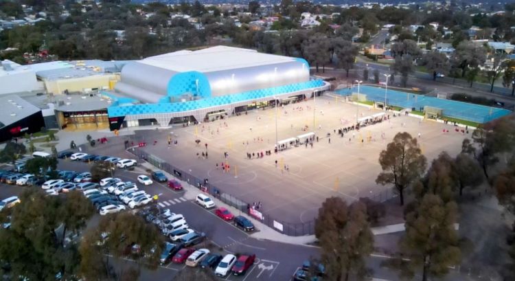 Artist's impression of Bendigo Stadium including the main buildings in the background and a carpark and people playing netball under lights in the foreground.