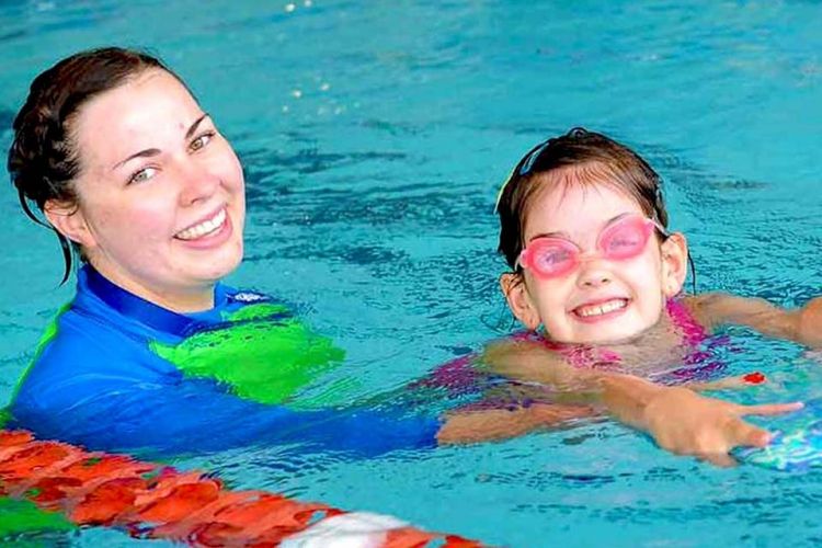 A swimming instructor helps a young girl wearing pink goggles learn to swim.