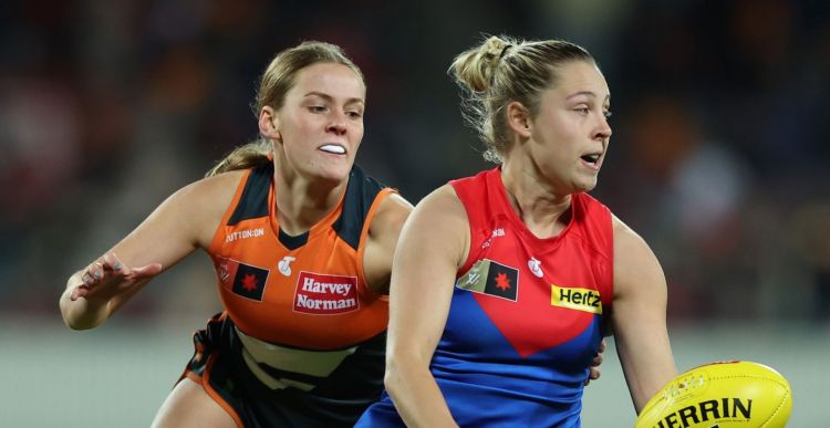A woman in a Greater Western Sydney jersey tackles a Melbourne player who is attempting a handball. 