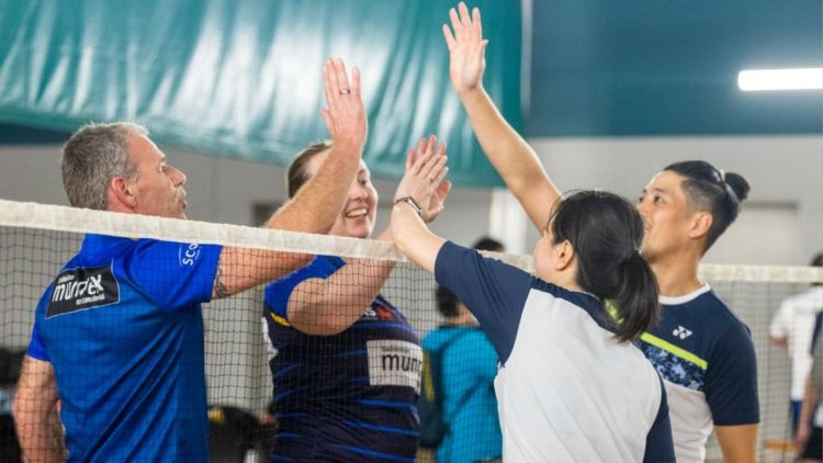 Two mixed doubles badminton teams high five over a net