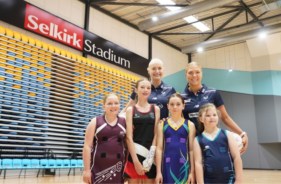 Melbourne Vixens players Kate Moloney and Jo Weston pose with junior netballers.