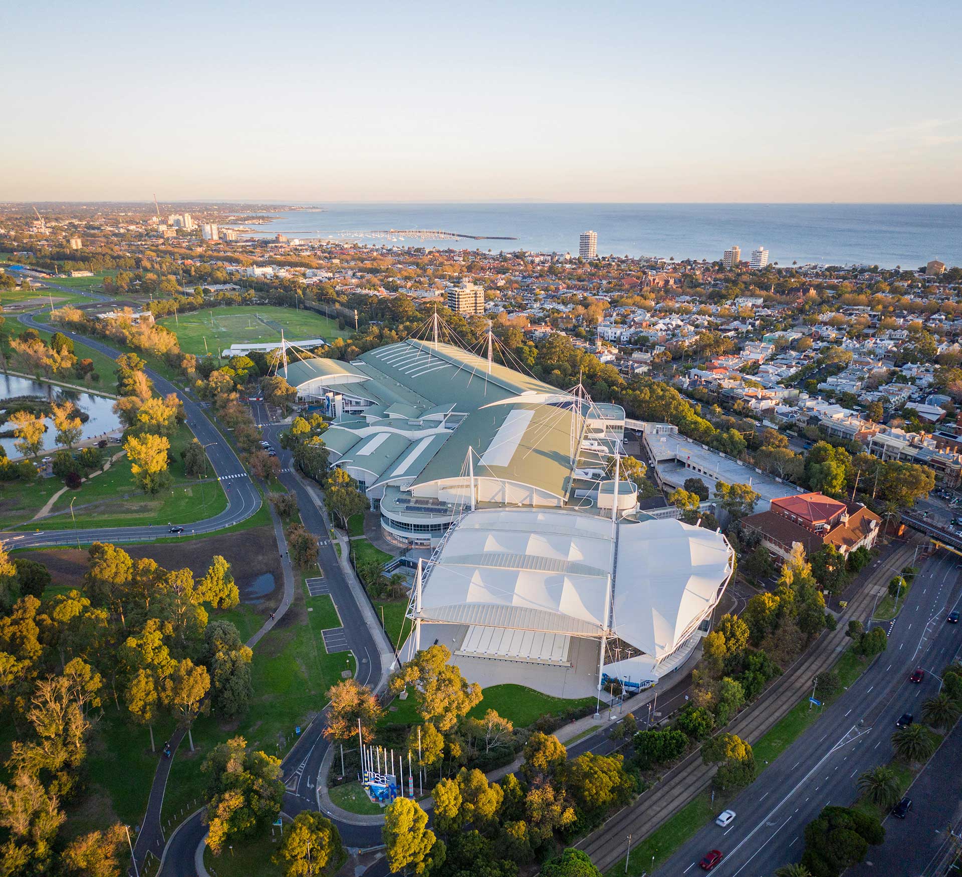 Aerial view of the Melbourne Sports and Aquatic Centre with Port Phillip Bay in the background.