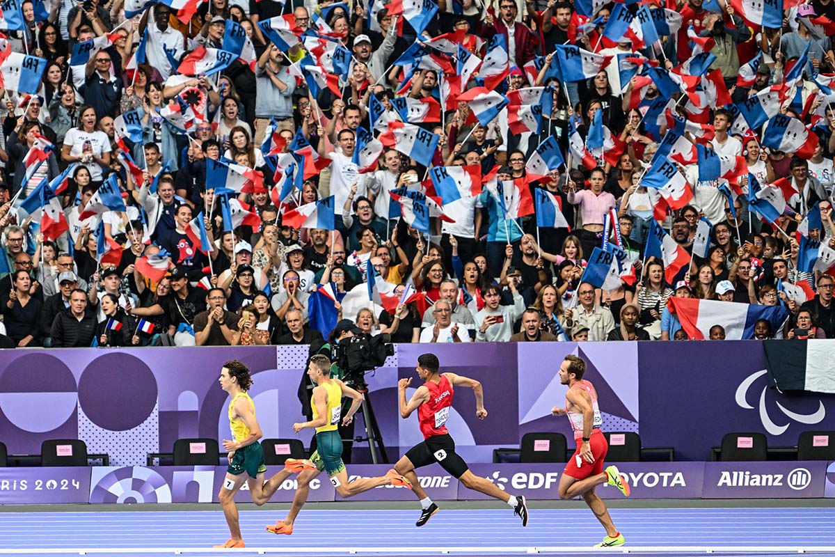 Reece and 3 other athletes run in front of crowd waving a sea of French flags.