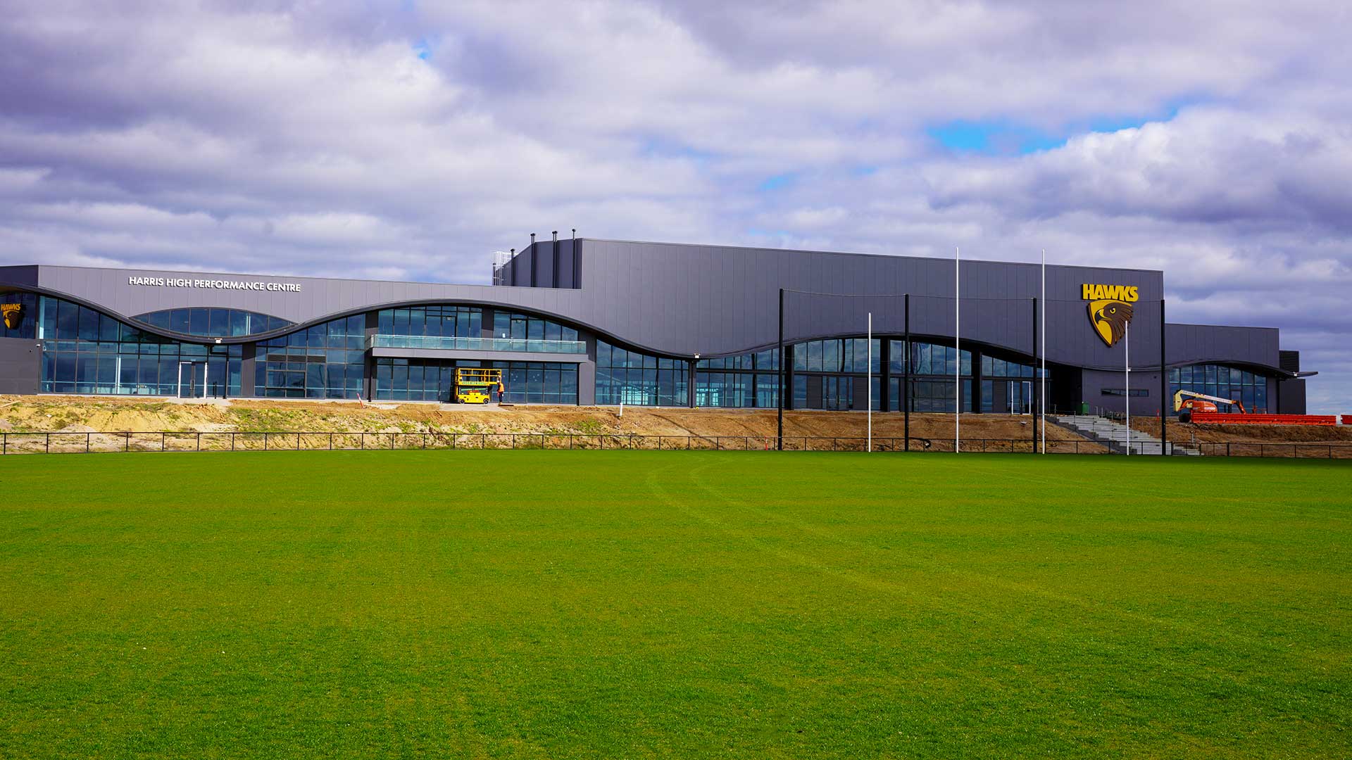 Image of the facade of the Kennedy Centre with a Hawks football team logo on the side of the building and the football ground in the foreground.